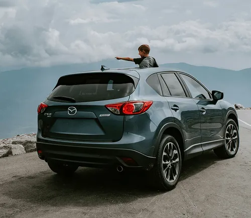 A man sitting on the back of a gray car.